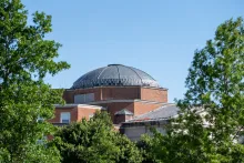 Dome of a building with red brick, surrounded by green trees, with blue sky above