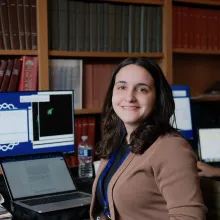 Laura Rodriguez smiles sitting in front of an open laptop and bookcases.