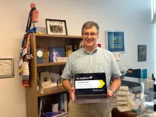 Mihai Pop holding a laptop and standing in front of a bookshelf in his office
