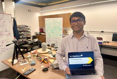 Nirupam Roy holding a laptop promoting his Reddit AMA in his lab