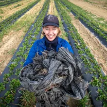 Krisztina Christmon holds a heap of agricultural plastics while standing in a field.