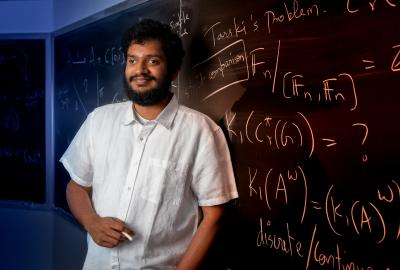 Srivatsav Kunnawalkam Elayavalli holding a piece of chalk and standing in front of a blackboard full of equations