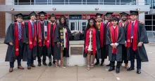 A group of graduates in regalia standing with a bronze Testudo statue. Credit: Mark Sherwood.