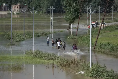 A group of people wading through a flooded road in Kashmir.