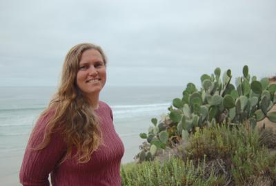 Jessica Goodheart standing on a beach by the water among cactus plants.