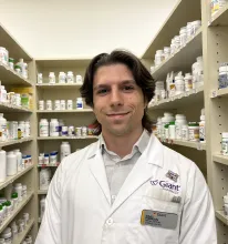 Isaac Robinson in a white lab coat in front of shelves of medications at Giant Pharmacy.
