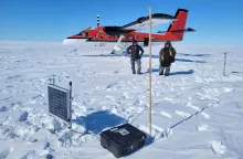 Associate Professor Nick Schmerr, left, with pilot Troy McKerral, behind a GPS station with a solar panel, recording unit, and antenna. The bamboo pole helps the retrieval team find the equipment, since the ice shelf can move a meter per day.