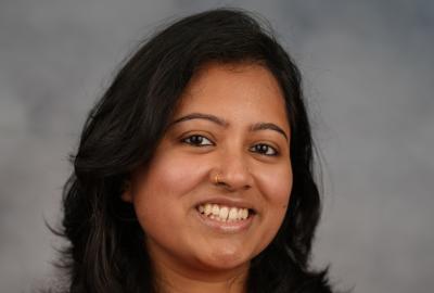 A headshot of a woman in an orange top standing in front of a mottled gray background.