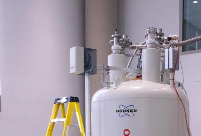 Large white Bruker Ascend 800 NMR magnet in a lab, with connected tubing and instruments; a yellow step ladder stands beside it.
