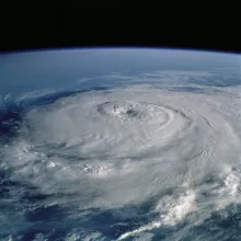 Aerial image of a hurricane from space, with white swirling clouds over a blue ocean.
