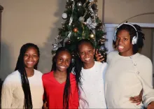 A family of four women stand in front of a Christmas tree wearing red and white sweaters.