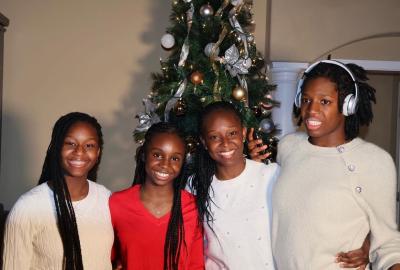 A family of four women stand in front of a Christmas tree wearing red and white sweaters.