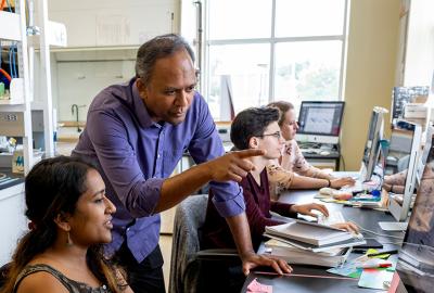 Antony Jose in his lab. He's talking to a group member while they are at a computer. In the background, other group members are working on computers as well. Credit: Lisa Helfert.