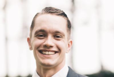 A man smiles wearing a black suit and yellow bow tie.