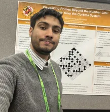 Samuel Márquez González wears a striped button down shirt and gray sweater, standing in front of his research poster which is white with orange headers.