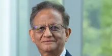 A headshot of a middle-aged man with glasses and a navy blue blazer against a soft, out-of-focus background.