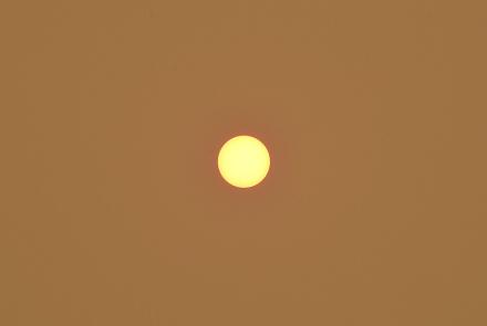 The sun appearing as a small yellow circle in the center of the image against a burnt orange sky.