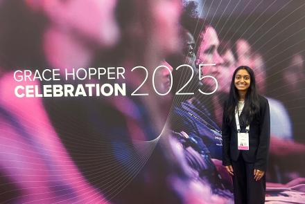 Nithika Ramanathan standing in front of the Grace Hopper Celebration 2025 banner