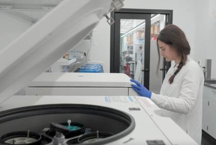 A person wearing blue gloves and a labcoat working in a lab