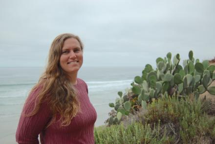 Jessica Goodheart standing on a beach by the water among cactus plants.