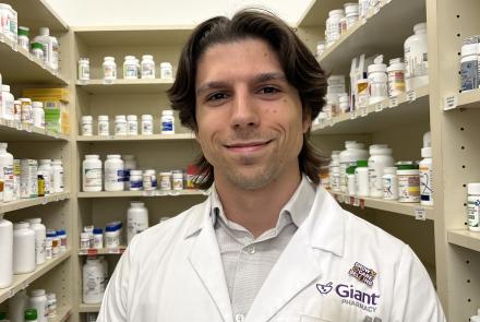 Isaac Robinson in a white lab coat in front of shelves of medications at Giant Pharmacy.