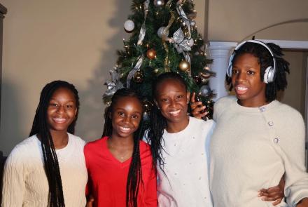 A family of four women stand in front of a Christmas tree wearing red and white sweaters.