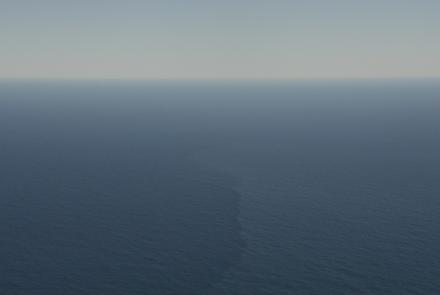 Aerial view of open ocean with a faint vertical streak marking a surface front amid calm blue water.