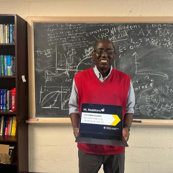 Mathematics Professor Abba Gumel standing in front of a chalkboard holding a laptop