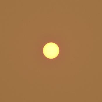 The sun appearing as a small yellow circle in the center of the image against a burnt orange sky.