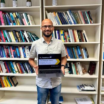 Pratyush Tiwary holding a laptop standing in front of several bookshelves