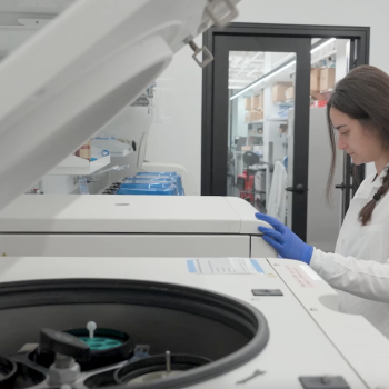 A person wearing blue gloves and a labcoat working in a lab