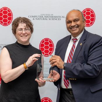 Two people holding an award in front of a CMNS step-and-repeat banner