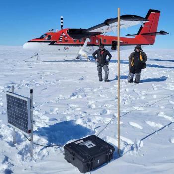 Associate Professor Nick Schmerr, left, with pilot Troy McKerral, behind a GPS station with a solar panel, recording unit, and antenna. The bamboo pole helps the retrieval team find the equipment, since the ice shelf can move a meter per day.