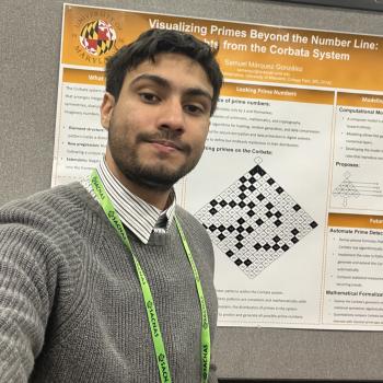 Samuel Márquez González wears a striped button down shirt and gray sweater, standing in front of his research poster which is white with orange headers.