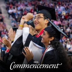 Two students in graduation regalia celebrating, with a blurred crowd in the background.