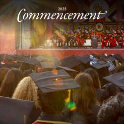 Photo of a large crowd of people at commencement. We see the students from the back, and ahead, a platform party facing the audience.
