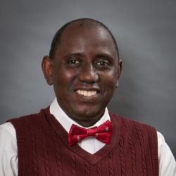 Abba Gumel smiling in a red sweater vest and red bow tie.