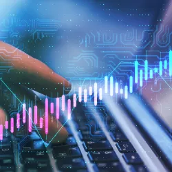 A close-up view of a person's hands typing on a laptop keyboard, overlaid with a glowing digital graphic of a rising financial stock chart, data points, and circuit board patterns in shades of blue, pink, and turquoise.