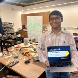 Nirupam Roy holding a laptop promoting his Reddit AMA in his lab