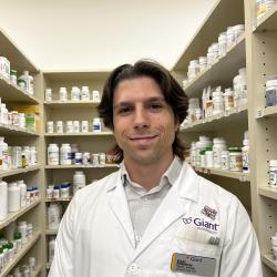 Isaac Robinson in a white lab coat in front of shelves of medications at Giant Pharmacy.
