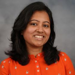 A headshot of a woman in an orange top standing in front of a mottled gray background.