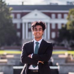 Dhruv Dewan stands in a suit in front of a red academic building.