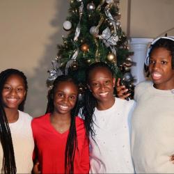 A family of four women stand in front of a Christmas tree wearing red and white sweaters.