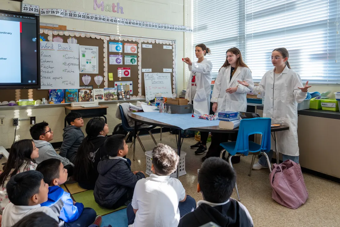 Three students leading a chemistry demonstration for a group of K-12 students