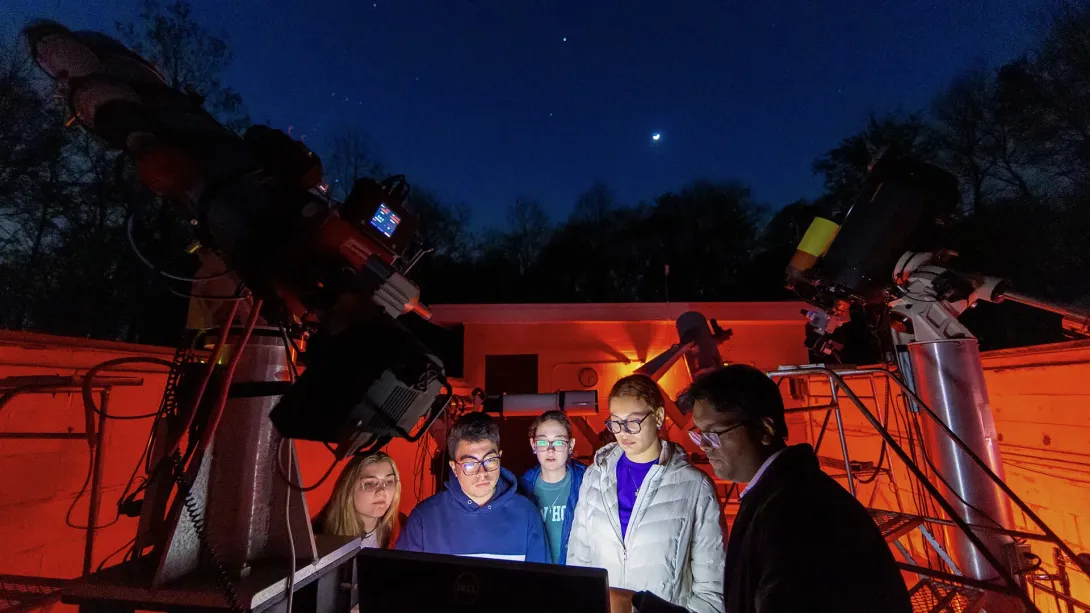 People gathered around a screen with the light illuminating their faces and a night sky in the background