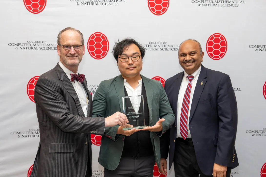 Three people holding an award in front of a step-and-repeat banner