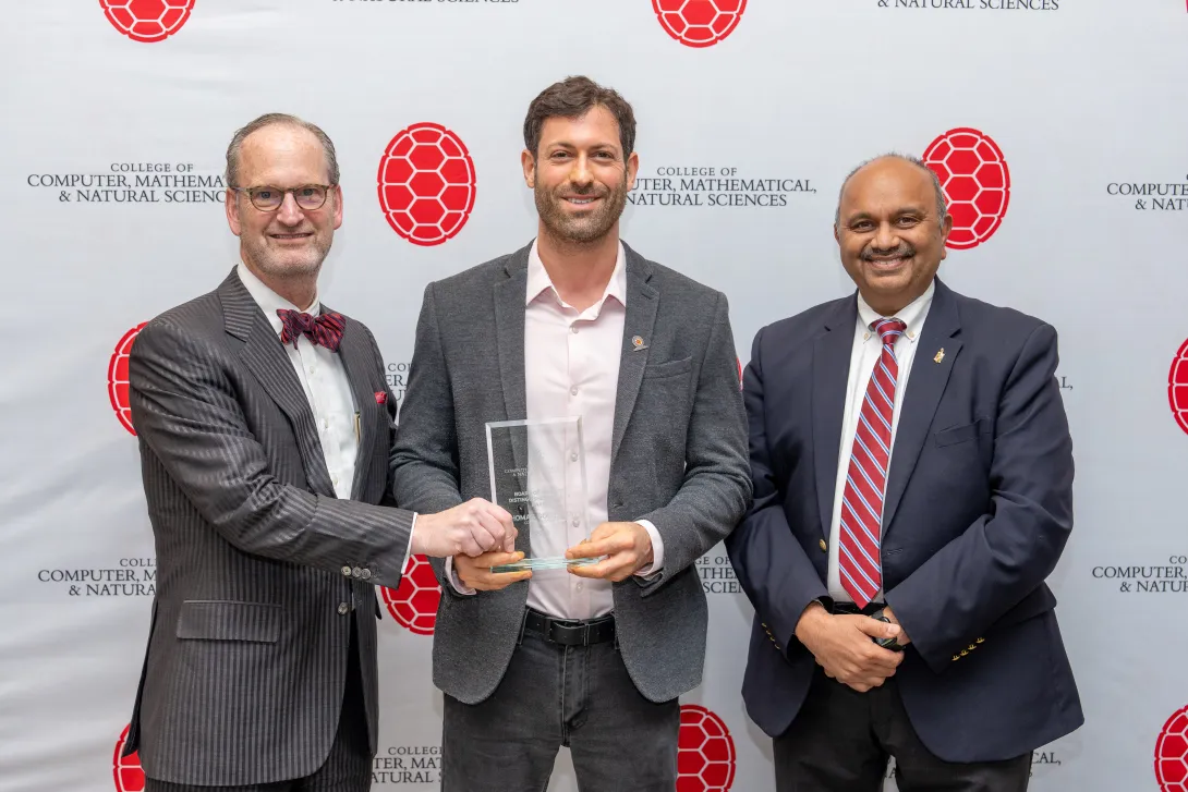 Three people holding an award in front of a step-and-repeat banner
