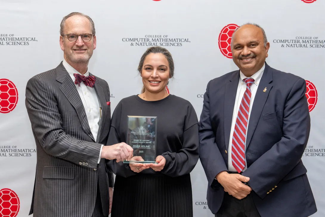 Three people holding an award in front of a step-and-repeat banner