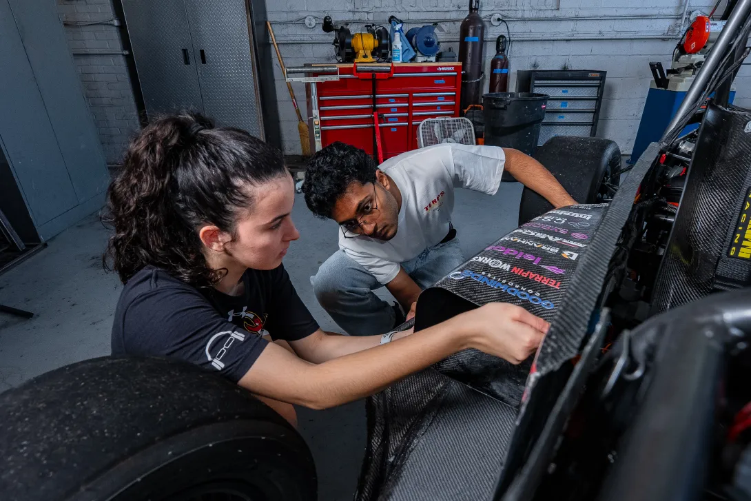 Two students inspect the body of the race car, with sponsor titles printed on it.