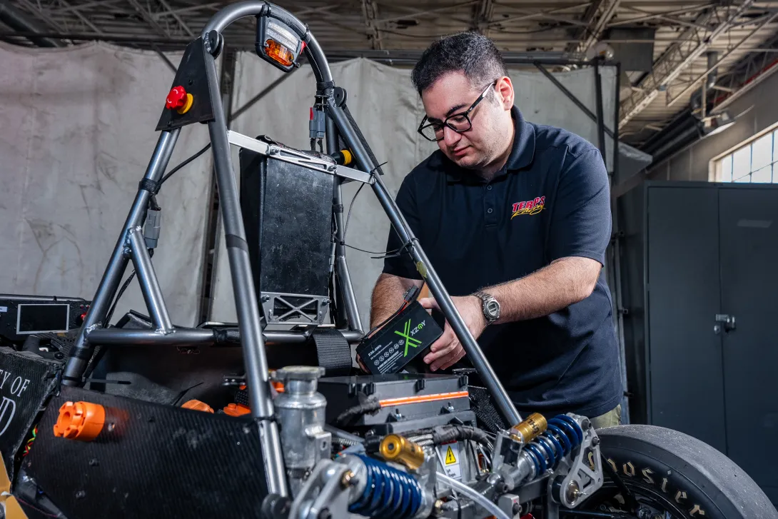 A student in a Terps Racing EV polo adjusts components on the car. 